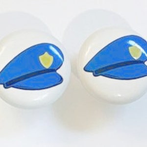 May include: Two white ceramic knobs with a blue and yellow police hat design.