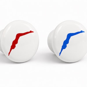 May include: Two round white ceramic cabinet knobs. One knob features a red silhouette of a person diving, while the other knob displays a blue silhouette of a person diving. Both knobs have a smooth, glossy finish and a standard circular shape.