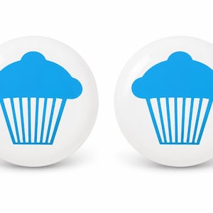 May include: Two circular white buttons, each featuring a bright blue graphic of a cupcake. The cupcake design displays a rounded top and a pleated base, centered on the smooth, glossy surface of each individual white button component.