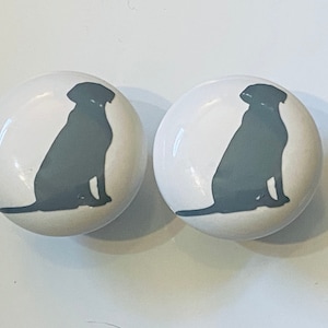 May include: Two white ceramic knobs with a gray silhouette of a dog sitting on each knob.