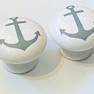 May include: Two white ceramic drawer knobs with a gray anchor design. The anchors are stylized with a simple, classic design.