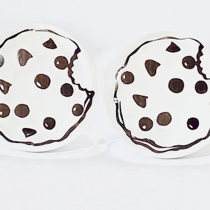 May include: Two white ceramic cookie-shaped earrings with a black outline and brown chocolate chips.