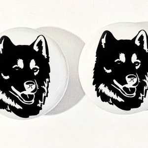 May include: Two white round buttons with a black silhouette of a husky dog's head on each button.
