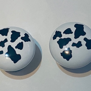 May include: Two white ceramic knobs with black cow print designs.