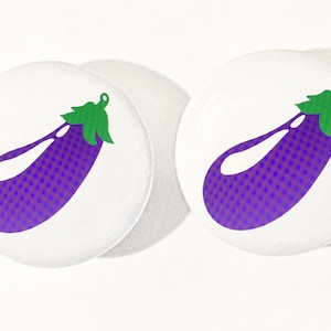 May include: Two white round buttons with a purple eggplant with a green stem on each button.