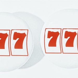 May include: Two white round coasters with red 7s printed on them. The 7s are in a slot machine style.
