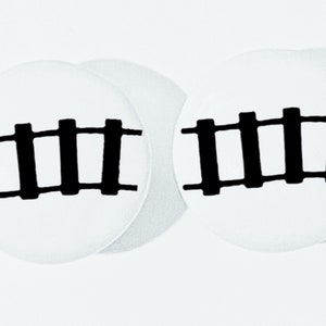 May include: Two white round coasters with a black railroad track design.