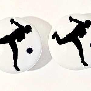 May include: Two white ceramic knobs with black silhouettes of a person throwing a ball. Each knob has a black circle representing the ball.