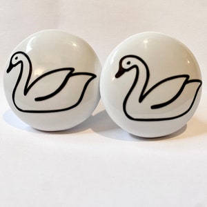 May include: Two white ceramic drawer knobs with black swan designs.