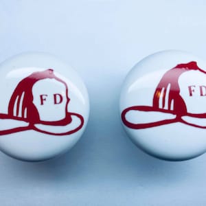 May include: Two white ceramic knobs with red firefighter helmet designs and the letters "FD" on each.