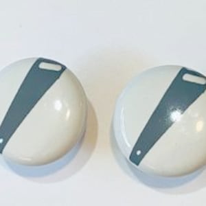 May include: Two white ceramic knobs with a gray saw blade design.