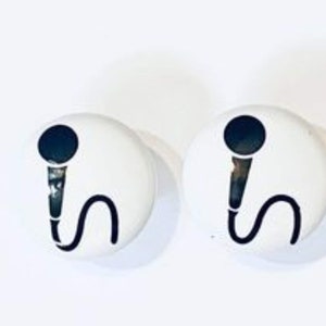 May include: Two white round buttons with a black microphone design. The microphone has a black handle and a curved black cord. The buttons are set against a white background.