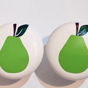 May include: Two white ceramic knobs with a green pear design. The pears have a brown stem and a green leaf.
