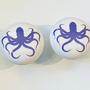 May include: Two white ceramic knobs with a purple octopus silhouette design.