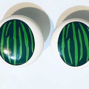 May include: Two white ceramic knobs with a green and black zebra stripe design.