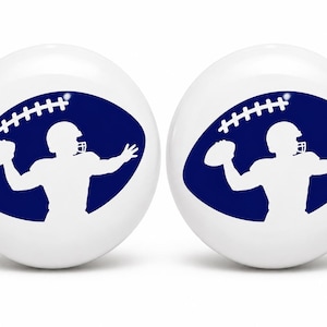 May include: Two white spherical objects featuring a dark blue oval graphic. Inside the oval is a white silhouette of a football player in a helmet preparing to throw a football, with a small football icon positioned above the player's head.