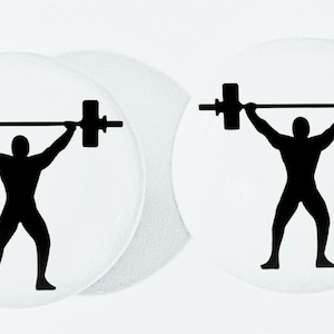 May include: Two white round coasters with a black silhouette of a person lifting a barbell.