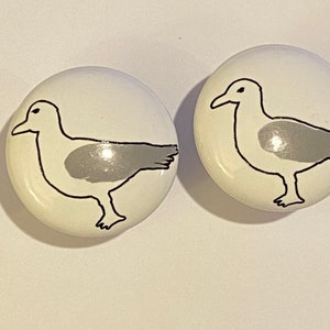 May include: Two white ceramic knobs with a black and gray seagull design.