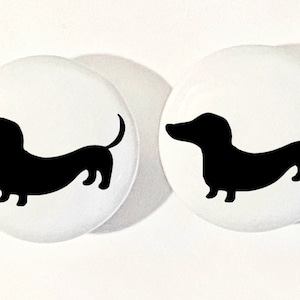 May include: Two white ceramic round knobs with a black silhouette of a dachshund dog on each.