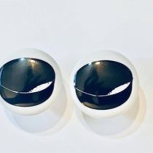 May include: Two white round buttons with black and white eye designs. The eyes are closed and have a white line across the middle.