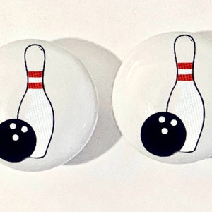 May include: Two white ceramic round knobs with a black bowling ball and a red and white bowling pin design.