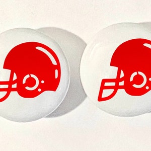 May include: Two white round buttons with a red football helmet graphic on each.