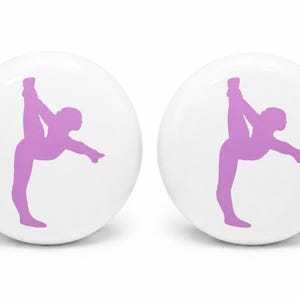 May include: Two round white knobs, each featuring a light purple silhouette of a gymnast performing a vertical split pose. The knobs have a smooth, glossy finish and a circular shape, displaying the same graphic design on both individual pieces.