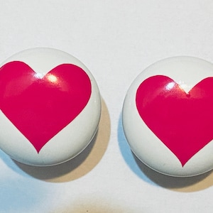 May include: Two white ceramic knobs with a pink heart design.