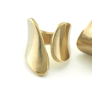 Puede incluir: Dos anillos de color dorado con un diseño abstracto único. Los anillos están hechos de metal y tienen un acabado liso y pulido.