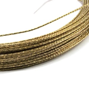 May include: A spool of gold metallic thread, tightly wound and secured with a white plastic tie. The thread has a textured, slightly sparkly appearance, reflecting light. Ideal for crafting and embellishments.