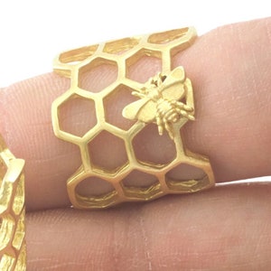 May include: Two gold-toned adjustable rings with a honeycomb design and a bee charm. The rings are open and can be adjusted to fit different finger sizes.
