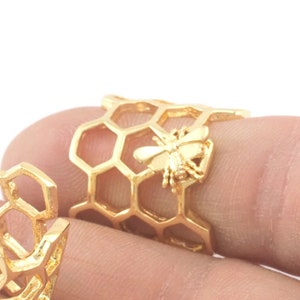 May include: Two gold-toned rings with a honeycomb design. One ring features a small bee charm.