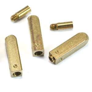 May include: Five gold-colored metal key blanks with a diamond-shaped indentation on the side. The key blanks are arranged in a scattered pattern on a white surface.