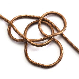 Puede incluir: Un collar de cadena de serpiente de color dorado. La cadena está retorcida y anudada, creando un patrón decorativo.