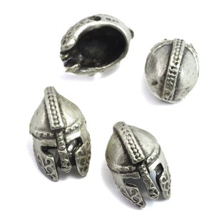 May include: Four silver-toned metal helmet charms. The charms are detailed with raised lines and designs. The charms are approximately 1 inch in diameter.