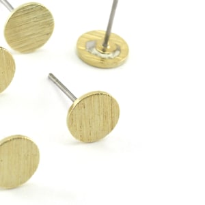 Peut inclure: Cinq boucles d'oreilles clous de couleur or avec une finition brossée. Chaque boucle d'oreille a un dessus rond et plat et une tige argentée.