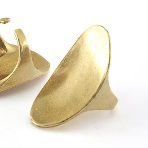 May include: Two gold-colored metal rings with a unique, asymmetrical design. The rings are smooth and have a slightly rounded shape.