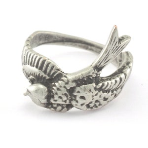 Könnte beinhalten: Ein silberner Ring mit einem detaillierten Design eines Vogels im Flug. Der Ring ist aus Metall und hat eine glatte Oberfläche.