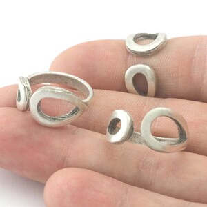 May include: Several silver-colored rings with an open teardrop design are displayed. The rings have a textured, matte finish. The rings are on a person's hand.