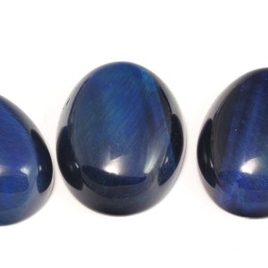 Può includere: Tre pietre lisce di occhio di tigre blu di forma ovale. Le pietre sono di colore blu scuro con sottili striature blu chiaro e nere.