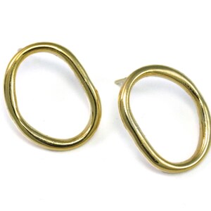 May include: A pair of gold-toned earrings with an irregular oval shape. The earrings are simple and modern.
