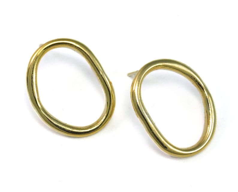 May include: A pair of gold-toned earrings with an irregular oval shape. The earrings are simple and modern.