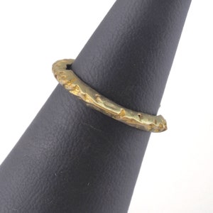 May include: A gold-toned ring with a textured, hammered finish. The ring is displayed on a black ring stand.