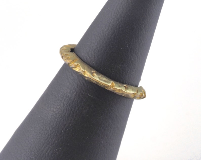May include: A gold-toned ring with a textured, hammered finish. The ring is displayed on a black ring stand.