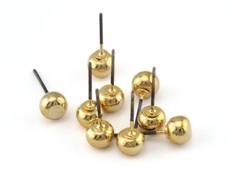 May include: A group of gold-colored earring posts with round tops. The posts are scattered on a white surface.