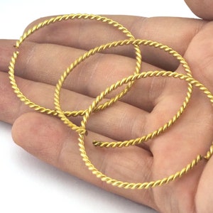 May include: Four gold-colored, twisted wire hoop earrings. The earrings are circular and have a textured, rope-like appearance. The hoops are held in a person's hand against a white background.