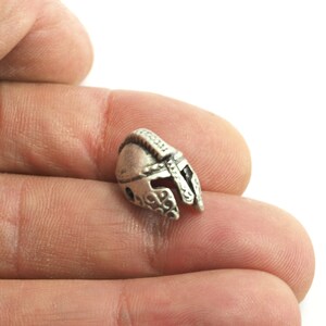 May include: A silver-colored metal charm in the shape of a helmet. The helmet has a detailed design and is a popular choice for jewelry making.