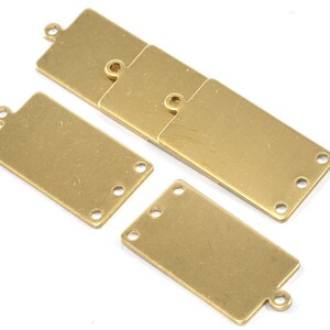 May include: Five gold-coloured metal rectangular tags with rounded corners and holes for attaching to a project. Each tag has three holes on each side.