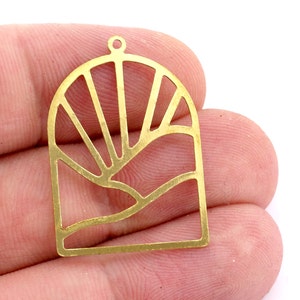 May include: Gold metal pendant featuring a cut-out design of a sun rising over a wavy line. The pendant has a hole at the top for hanging.