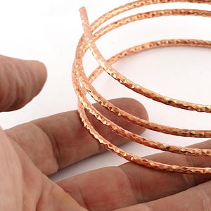 Peut inclure: Une longueur de fil de cuivre métallique enroulée présentant une surface texturée et facettée. Le fil est enroulé en plusieurs boucles circulaires, affichant une finition brun rougeâtre brillante et réfléchissante sur toute sa longueur.